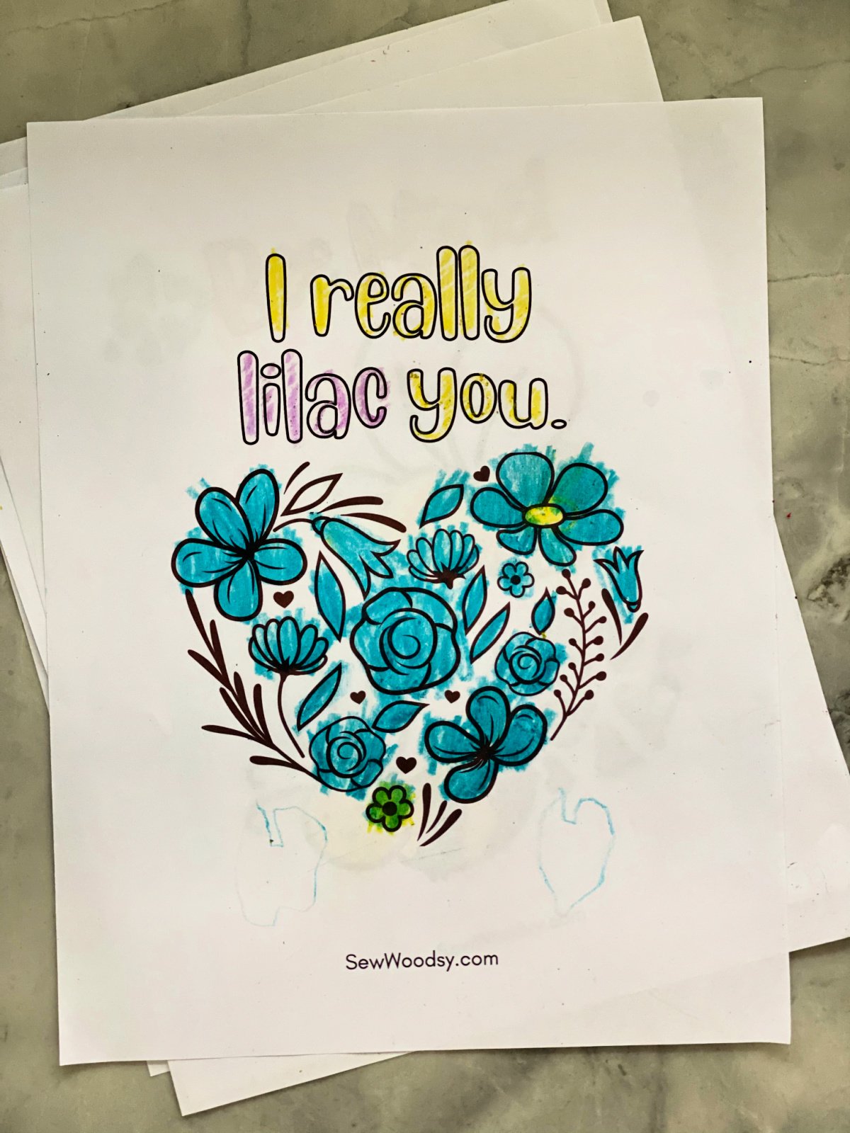 Heart shaped by flowers on a white paper colored in with the words "I really lilac you."