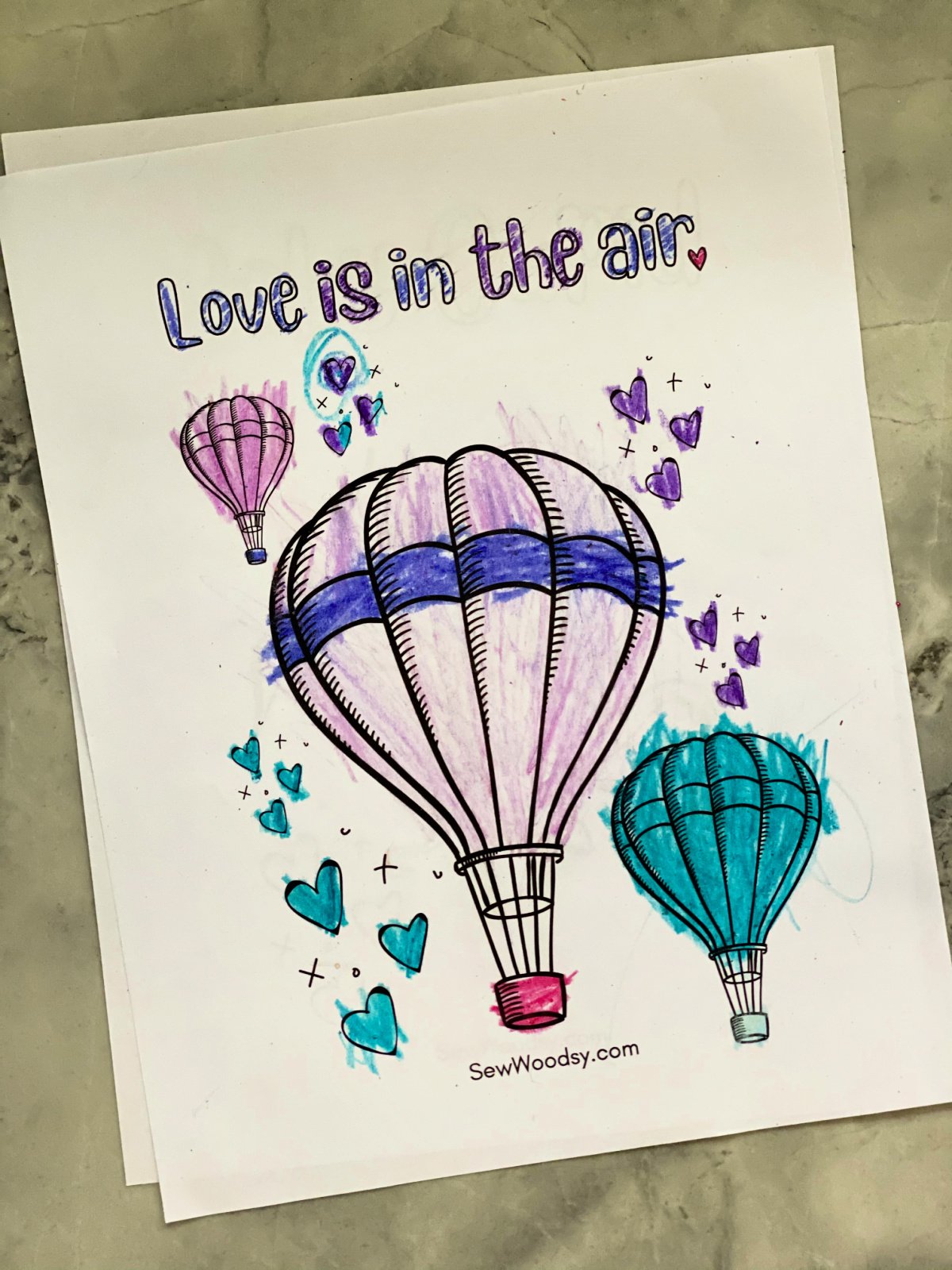 Three hot air ballons colored in on a white piece of paper with the words "love is in the air."