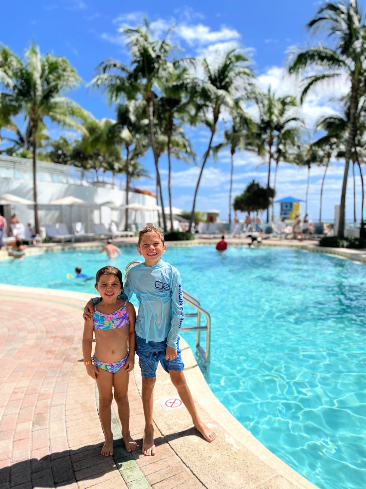 Two children standing next to a pool.