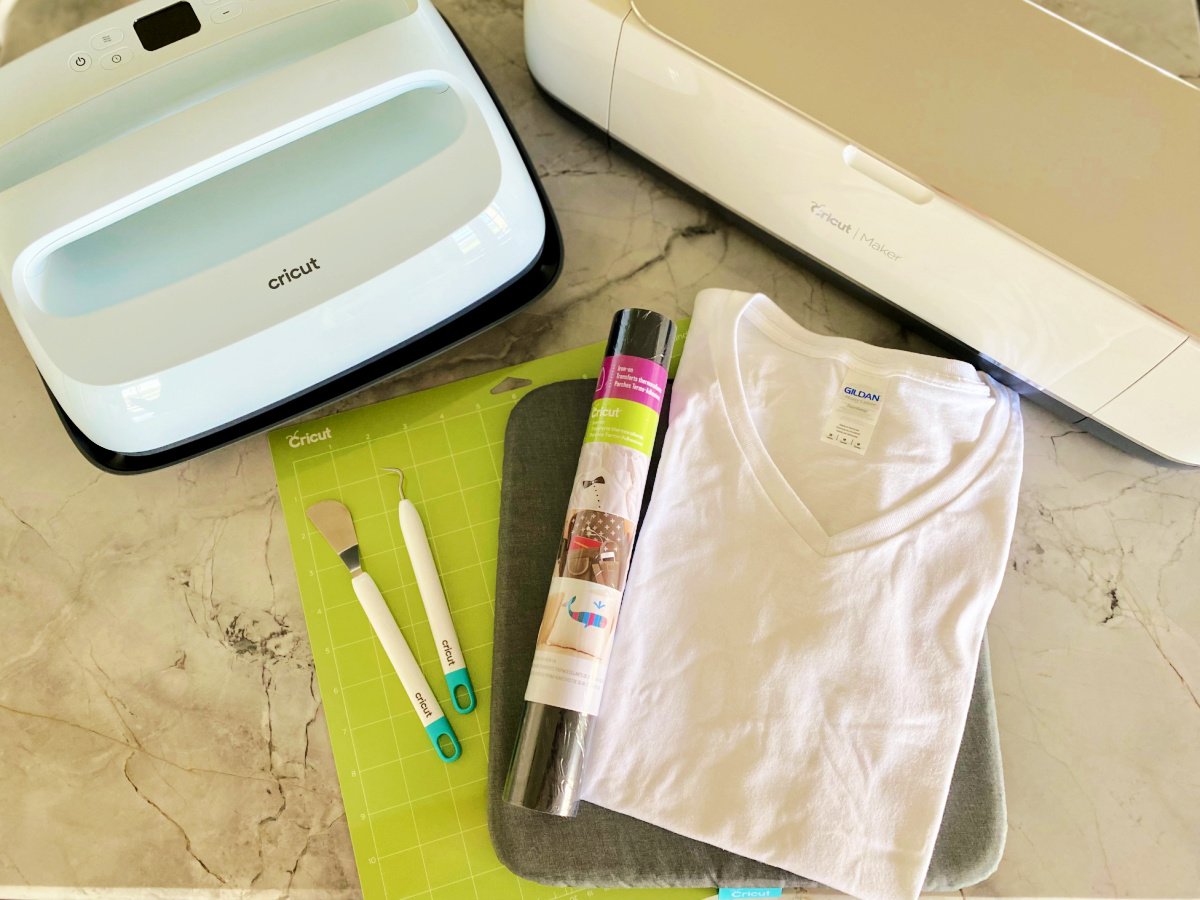 Supplies on counter; Cricut EasyPress, Cricut Maker, green mat, spatula, weeding tool, tshirt, and iron on vinyl.