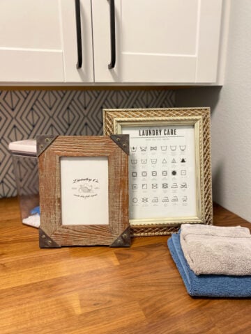 Brown frame and gold frame on a wood countertop with towels stacked in front.