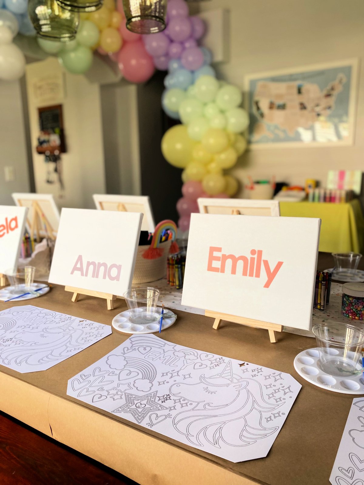 Two canvasses with coloring placemat and rainbow balloon arch in the background.