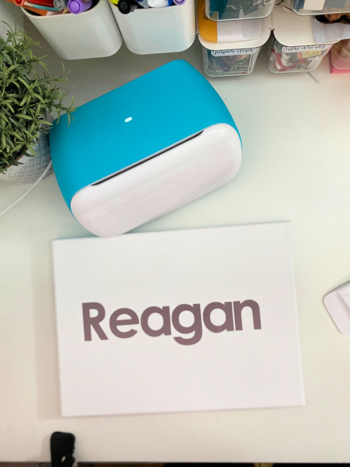 Cricut Joy on a white table with a canvas with vinyl that says "Reagan".