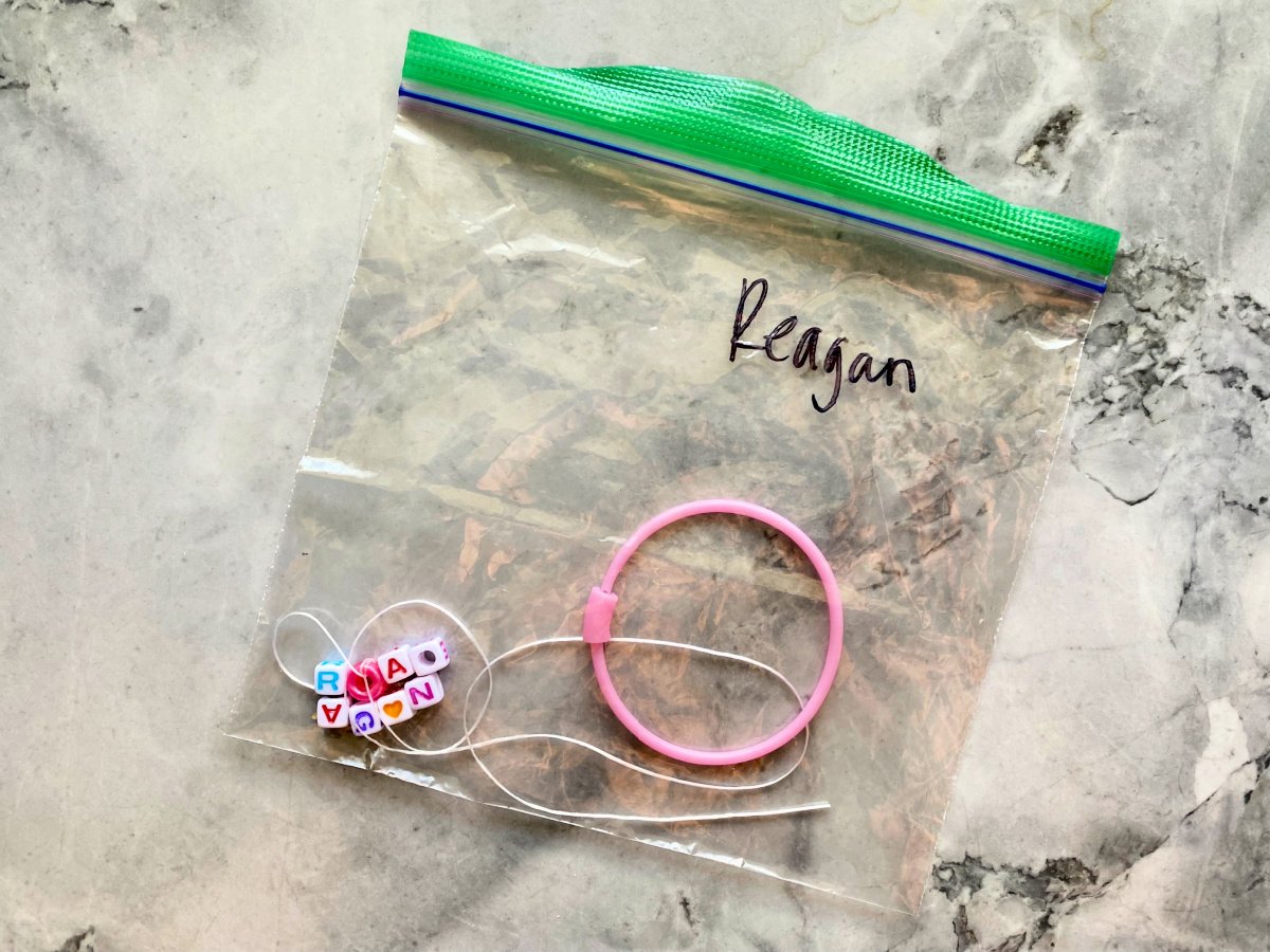 Bag with the name "reagan" with a pink round bracelette with necklace thread and lettered beads.