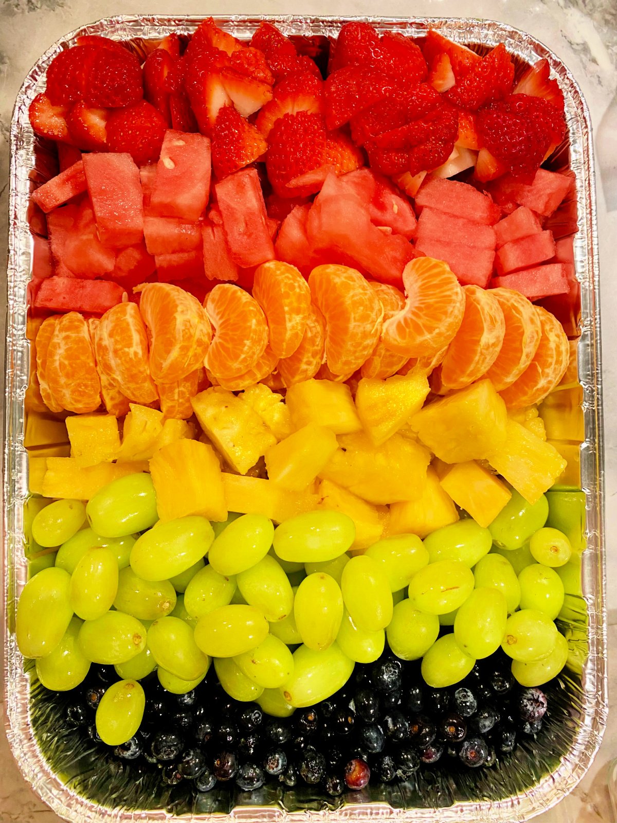 Rainbow fruit tray with strawberry, watermellon, oranges, pineapple, green grapes, and bueberries.