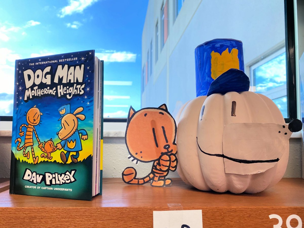 Cream colored dog man pumpkin with a little orange cat next to it with a Dog Man book next to it.