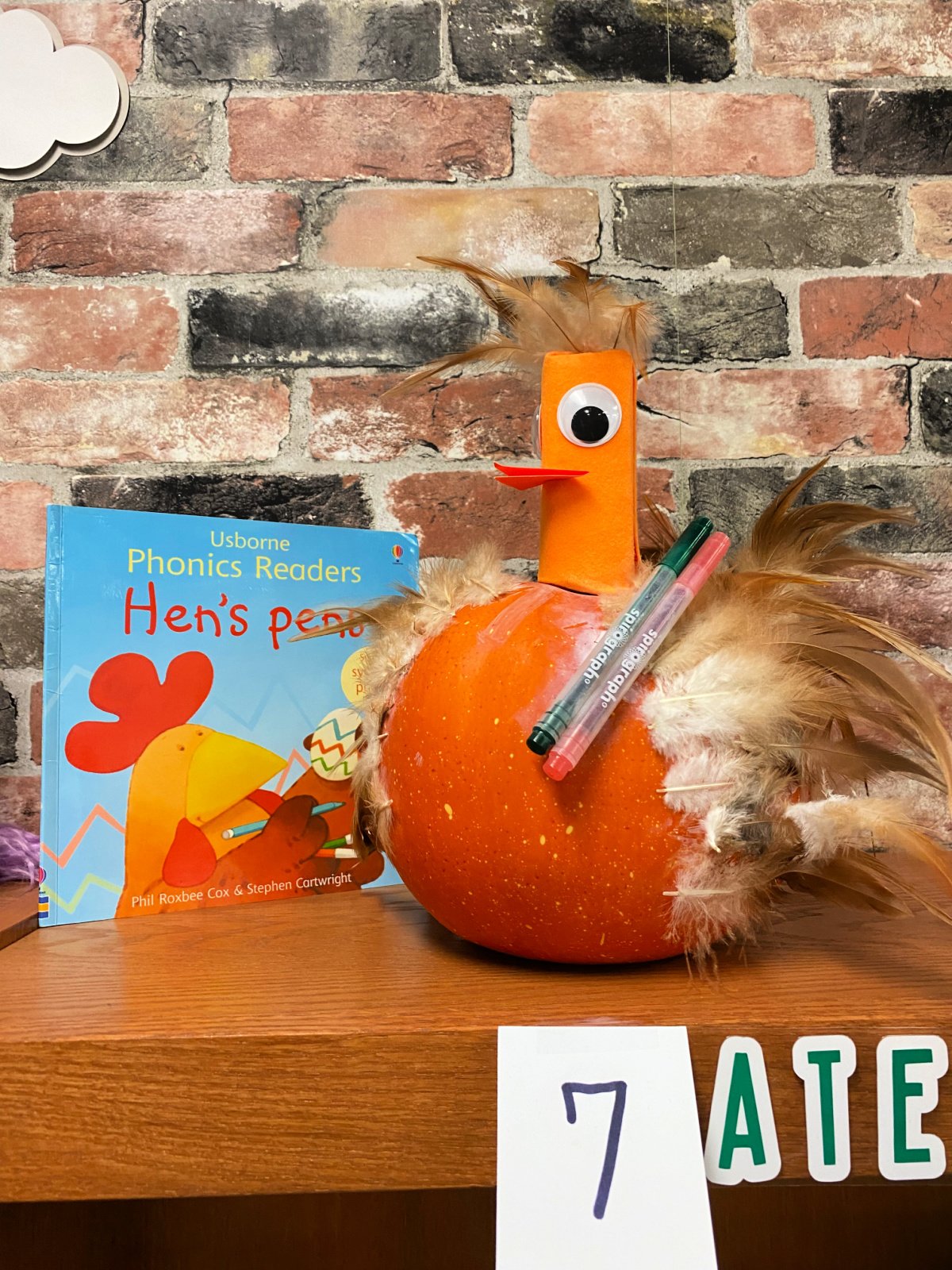 Orange pumpkin made as a hen with two pens on the pumpkin with a book next to it.