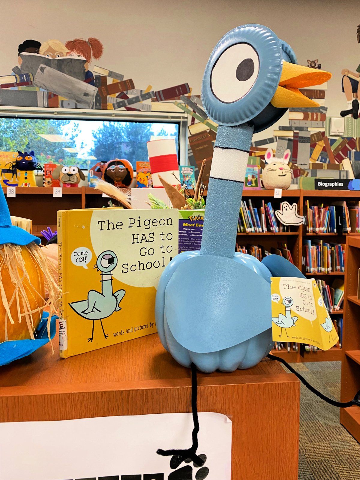 Blue pigeon made out of a pumpkin and pool noodle next to a yellow book.