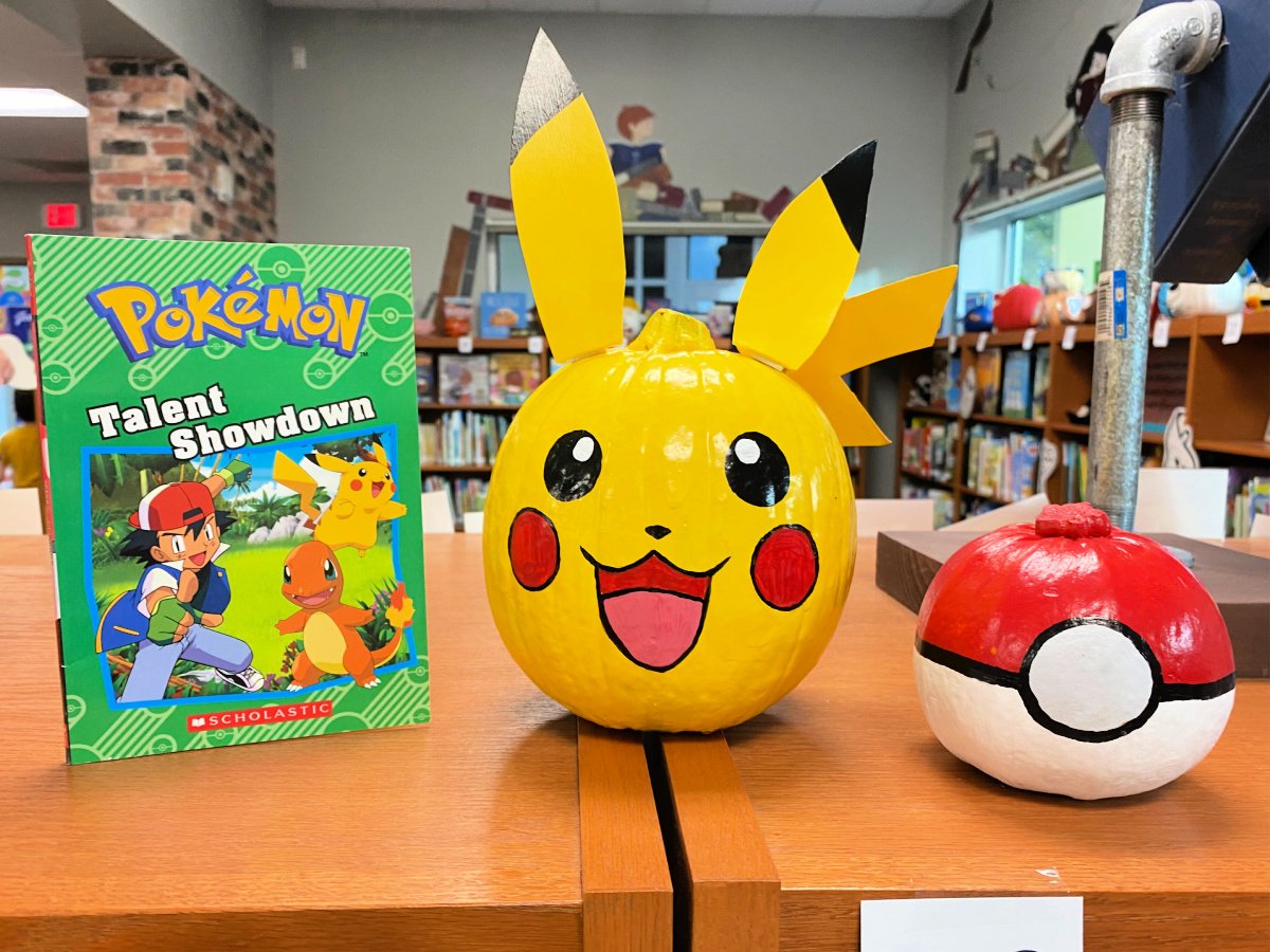 Yellow pikachu pumpkin with a red and white poke ball pumpkin and a Pokemon book next to it.