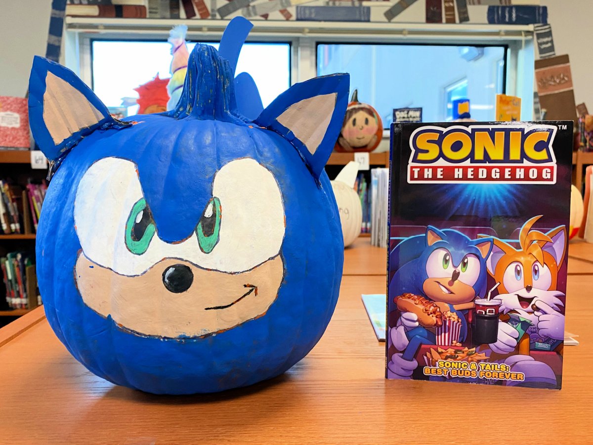 Blue sonic pumpkin on a wooden shelf next to a Sonic the Hedgehog book.