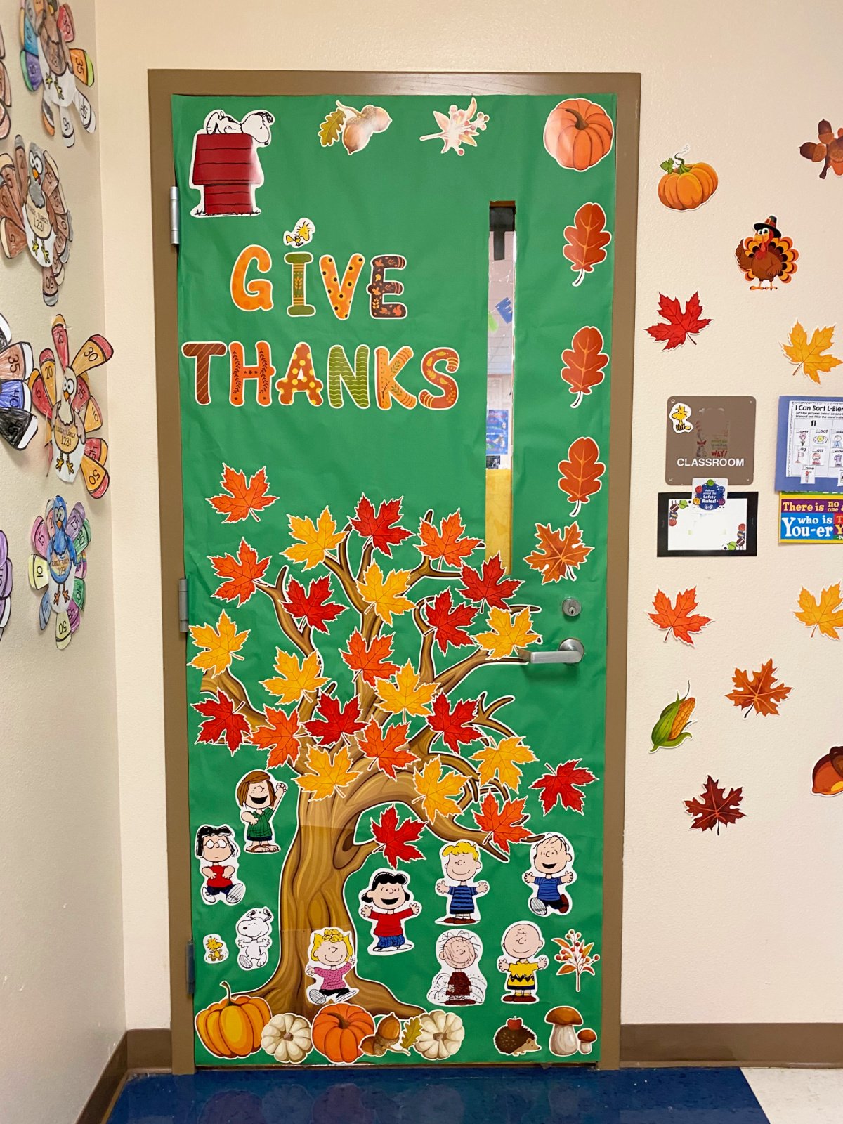 Green decorated door with a tree, fall leaves, and charlie brown characters.