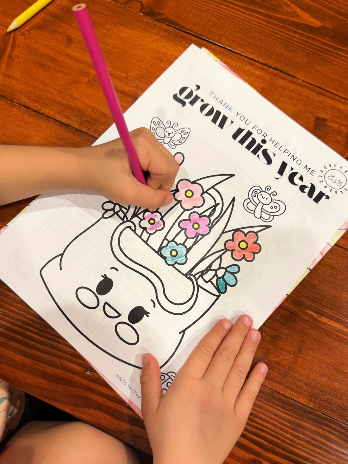 Little girl coloring a plant coloring page on a wood table.